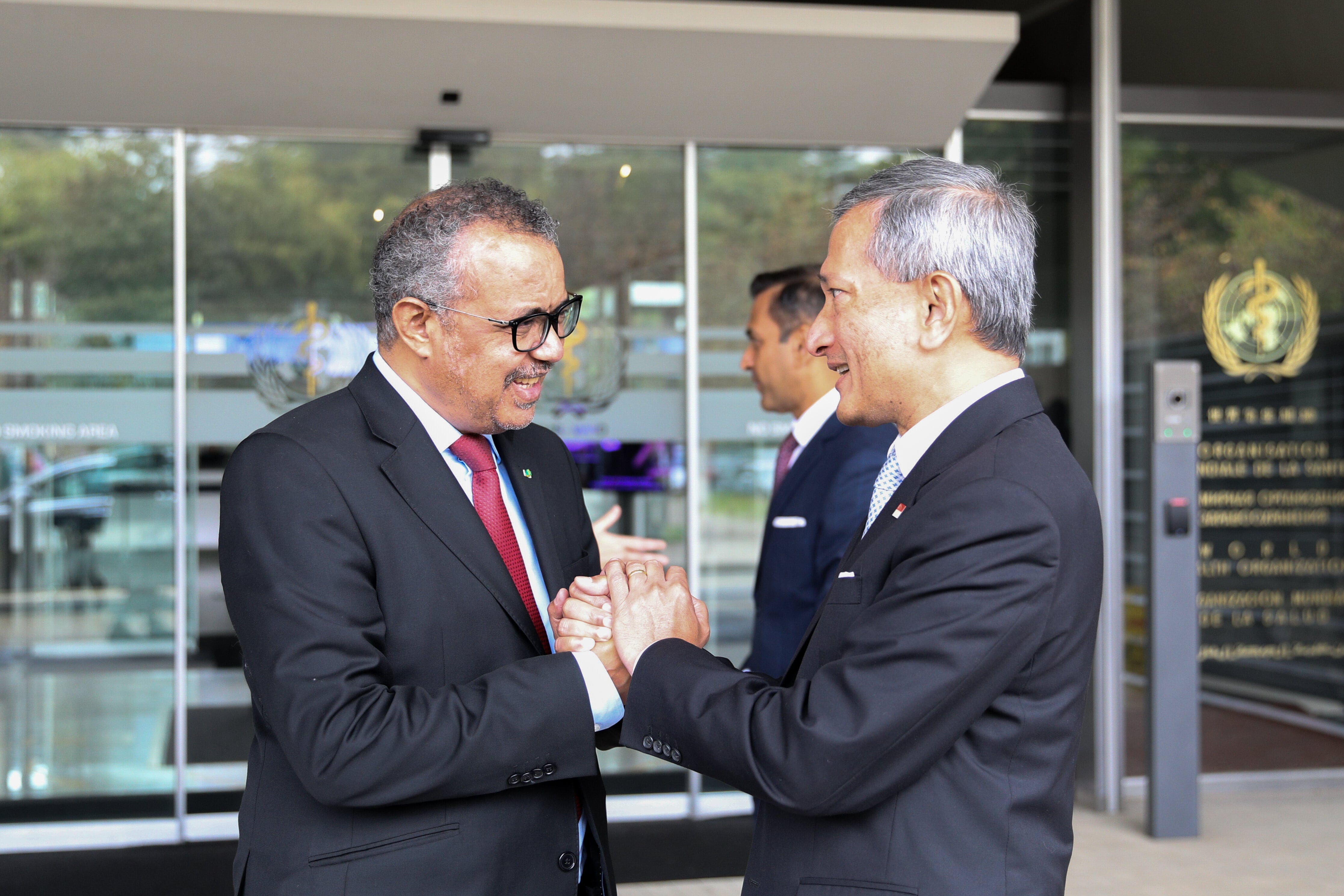 Tedros Adhanom Ghebreyesus shakes hands with an Asian man in front of the WHO building.